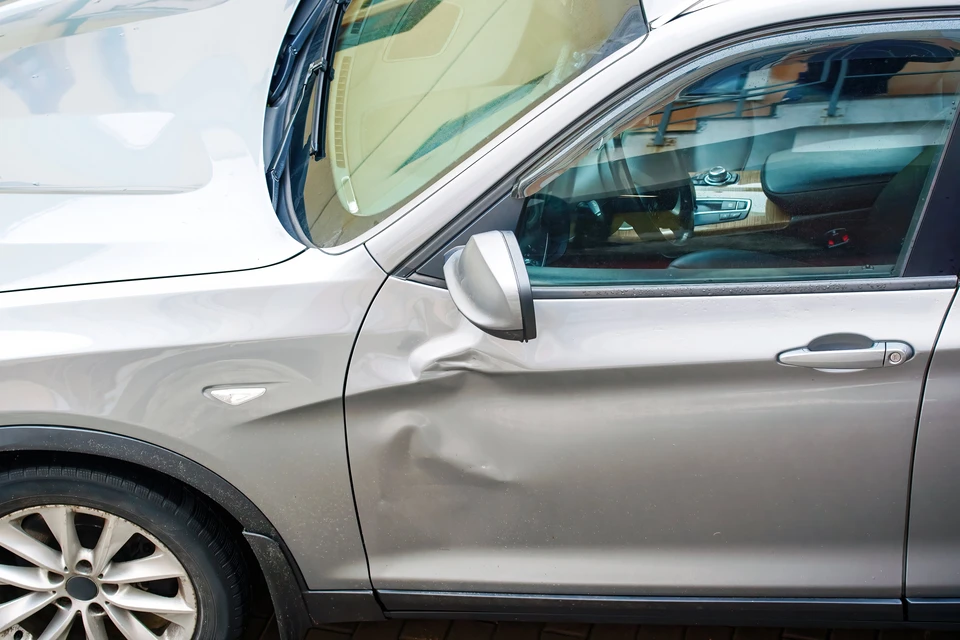 Un homme examine attentivement la carrosserie d'un véhicule en passant sa main sur la surface métallique peinte
