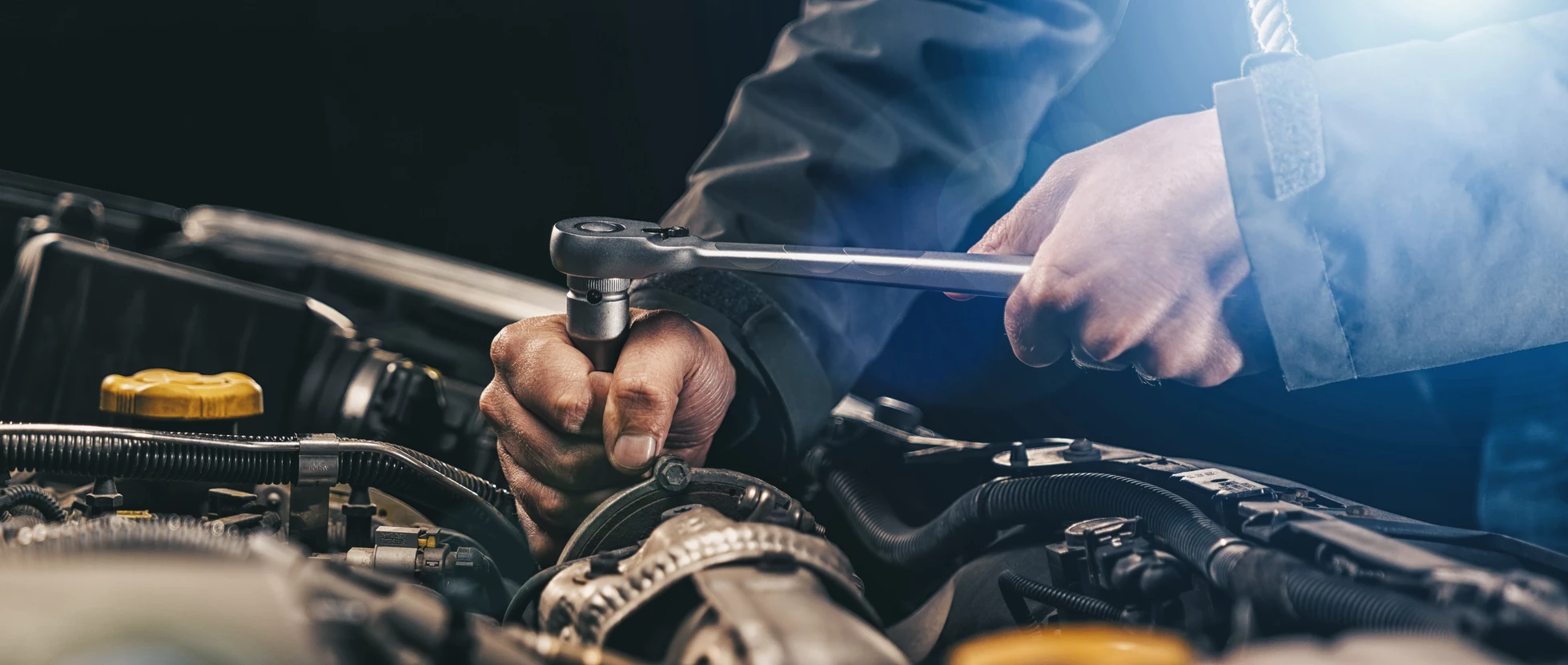Mécanicien automobile travaillant sous le capot d'un véhicule, utilisant une clé à cliquet pour serrer ou desserrer des composants mécaniques