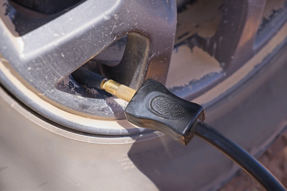 Main de personne inspectant de près un pneu automobile noir, doigt posé sur la bande de roulement usée présentant des traces d'usure visibles