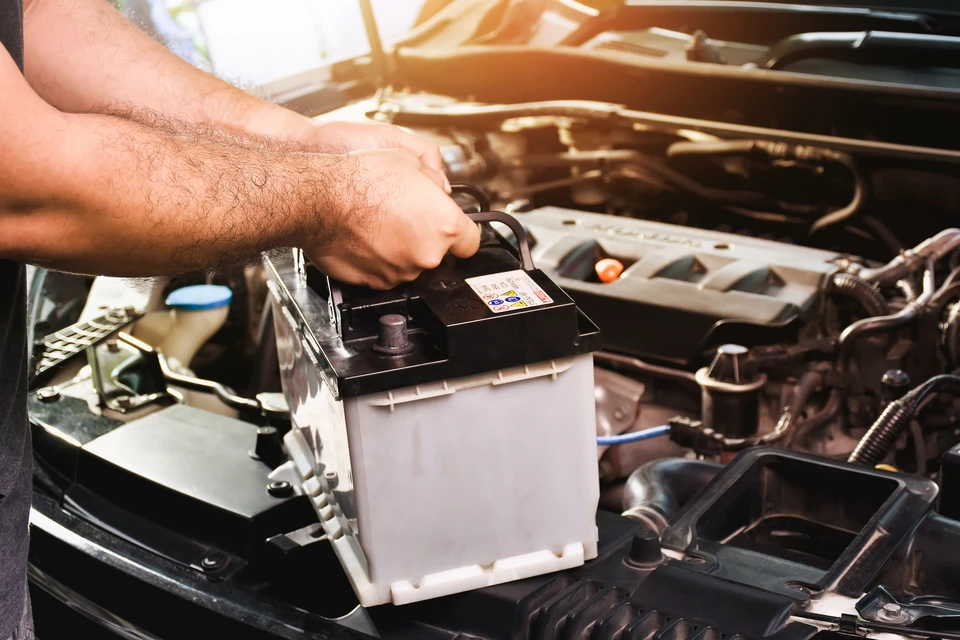 Photographe professionnelle montrant un technicien de dépannage automobile en uniforme, portant un gilet haute-visibilité, en action auprès d'une voiture particulière en détresse sur le bord d'une route. Le technicien effectue un diagnostic ou un remplacement de batterie, avec le camion de dépannage visible en arrière-plan. La scène doit transmettre une impression de professionnalisme, de fiabilité et de disponibilité immédiate pour aider le client.