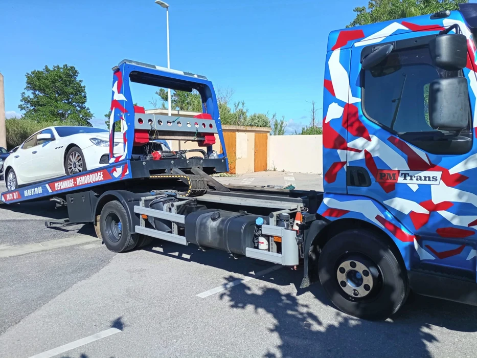 Camion dépanneuse PM Trans aux couleurs bleu, blanc, rouge avec motif géométrique abstrait, transportant un 4x4 tout-terrain type Jeep Cherokee sur plateau basculant