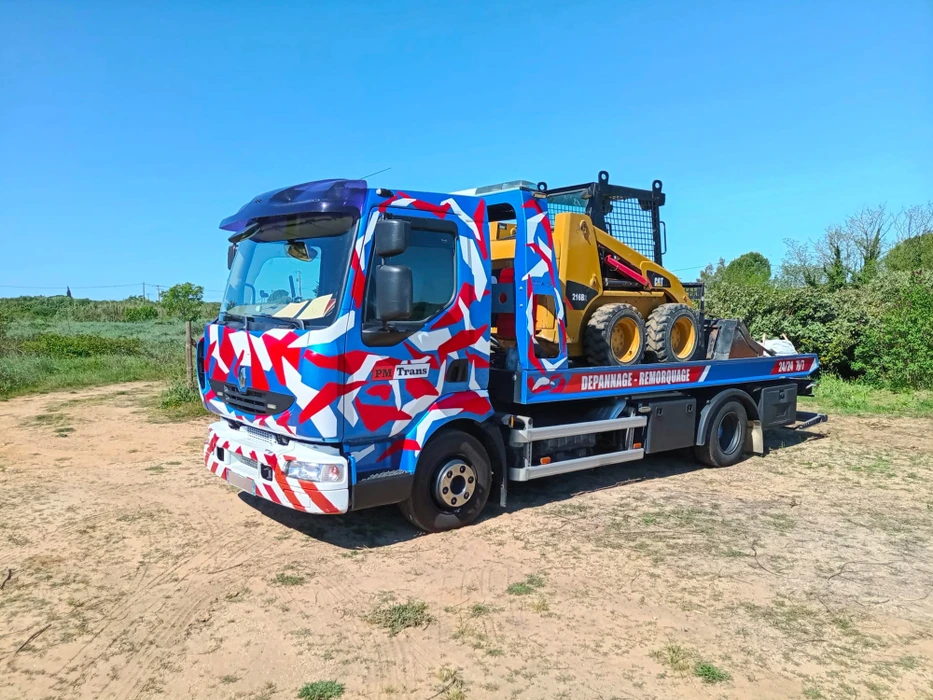 Camion dépanneuse plateau PM Trans aux couleurs vives rouge, blanc et bleu en camouflage géométrique, transportant une Renault Captur blanche accidentée, capot arraché exposant le groupe motopropulseur